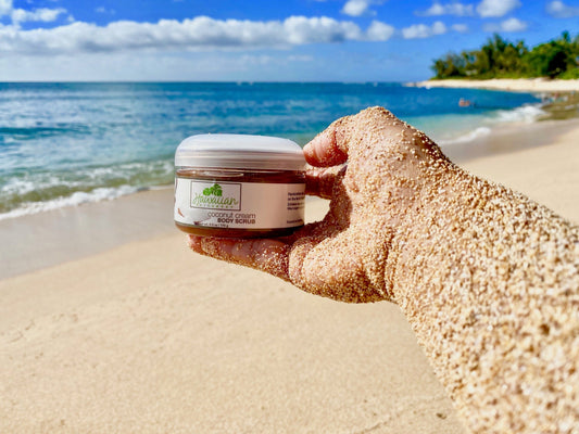 a jar of sugar body scrub held by a sandy outstretched arm at the beach. 